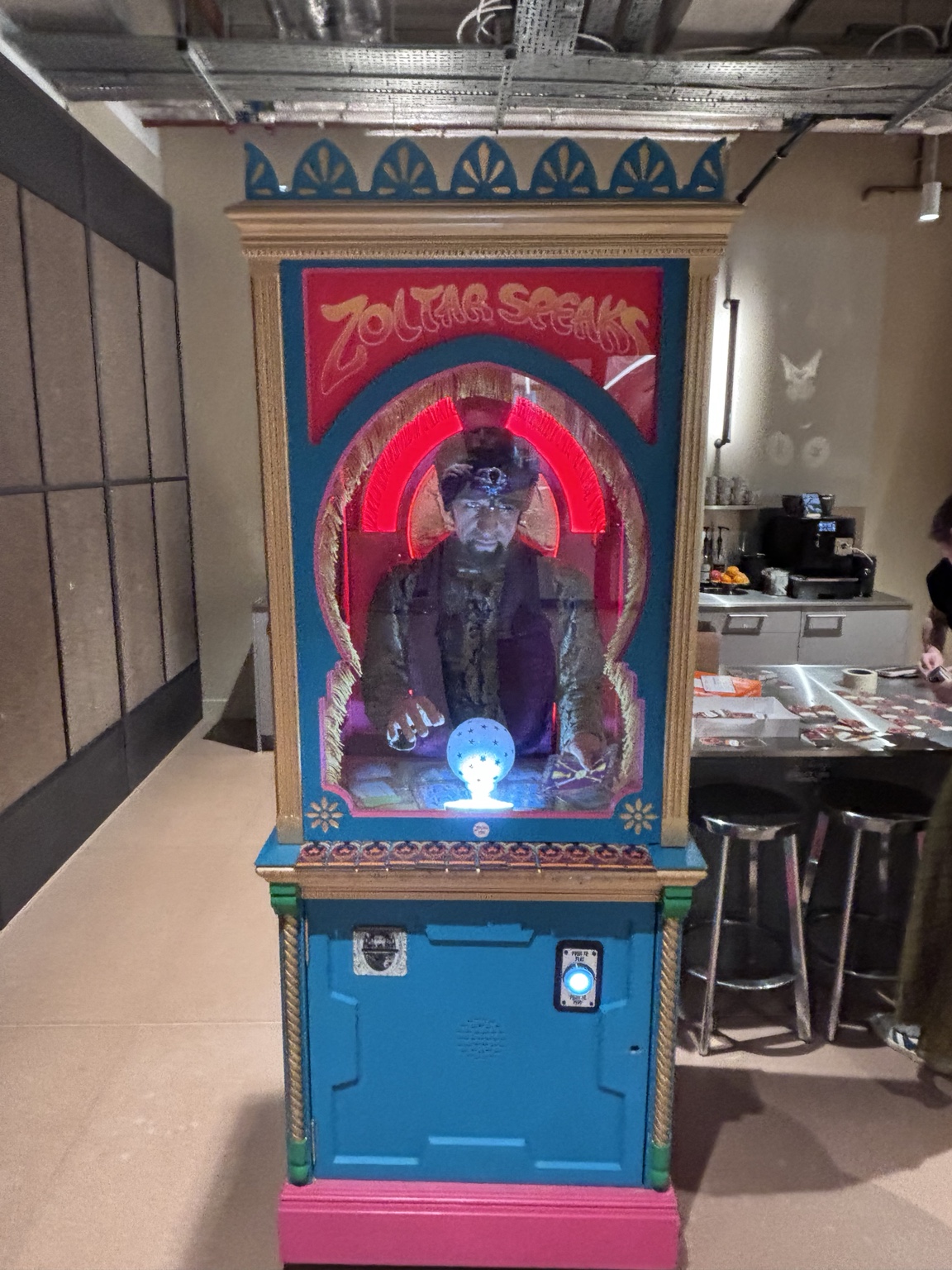 Colorful Zoltar fortune-telling arcade cabinet with a glass case and a figure inside, illuminated by red neon arches.