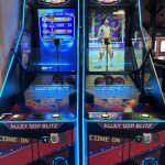 Pair of Alley Oop Blitz arcade basketball machines with blue neon lighting and hoops, facing forward in a gaming arcade.